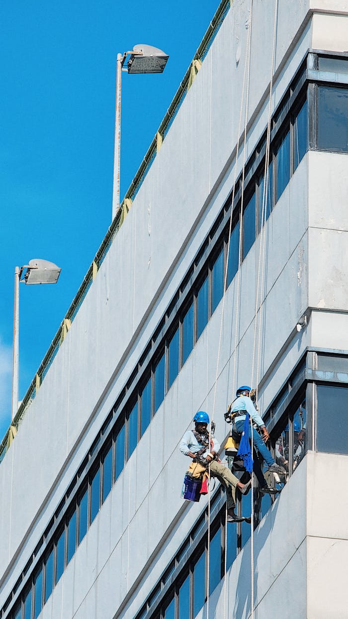 home-services-004 Professional window cleaners safely suspended on the facade of a modern building in Singapore.