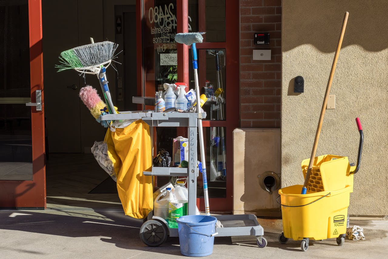 cta-bg Cleaning supplies and tools outside a building entrance bathed in sunlight.