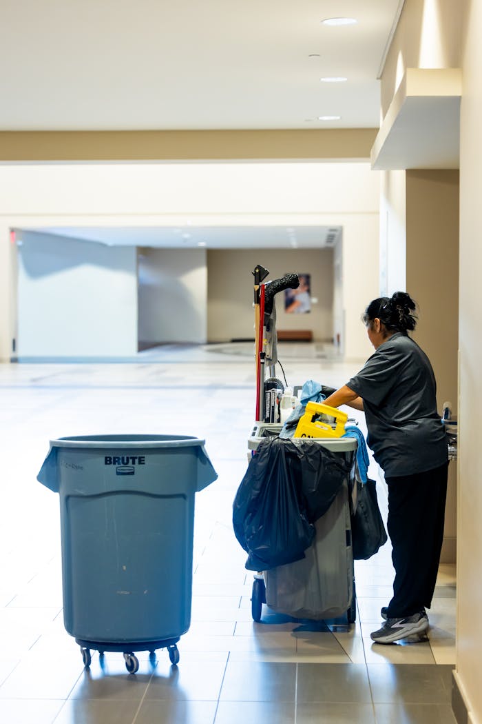 home-services-03 A janitorial worker pushes a cleaning cart in a spacious indoor hallway.